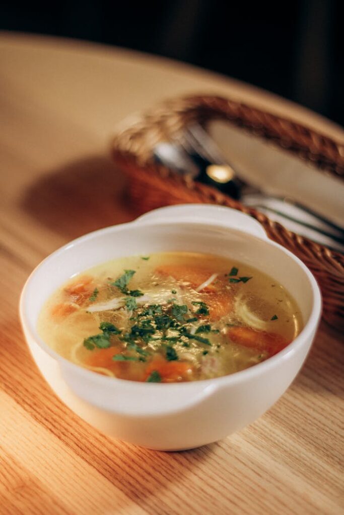 A comforting bowl of chicken noodle soup garnished with fresh herbs, perfect for a cozy meal.