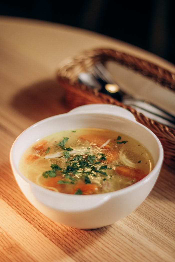 A comforting bowl of chicken noodle soup garnished with fresh herbs, perfect for a cozy meal.